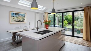 A modern kitchen with a central island, a dining area, and a large sliding glass door leading to a garden. - Idyllic Elegance, by Veeve (London)