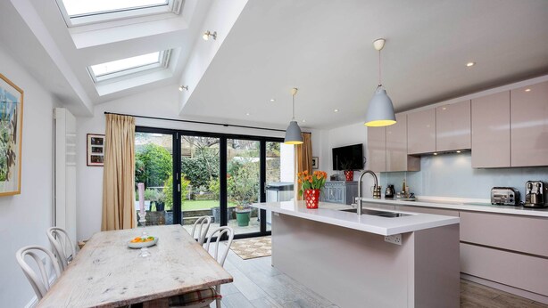 A modern kitchen with a central island, large windows, and a dining area with a table and chairs. - Idyllic Elegance, by Veeve (London)
