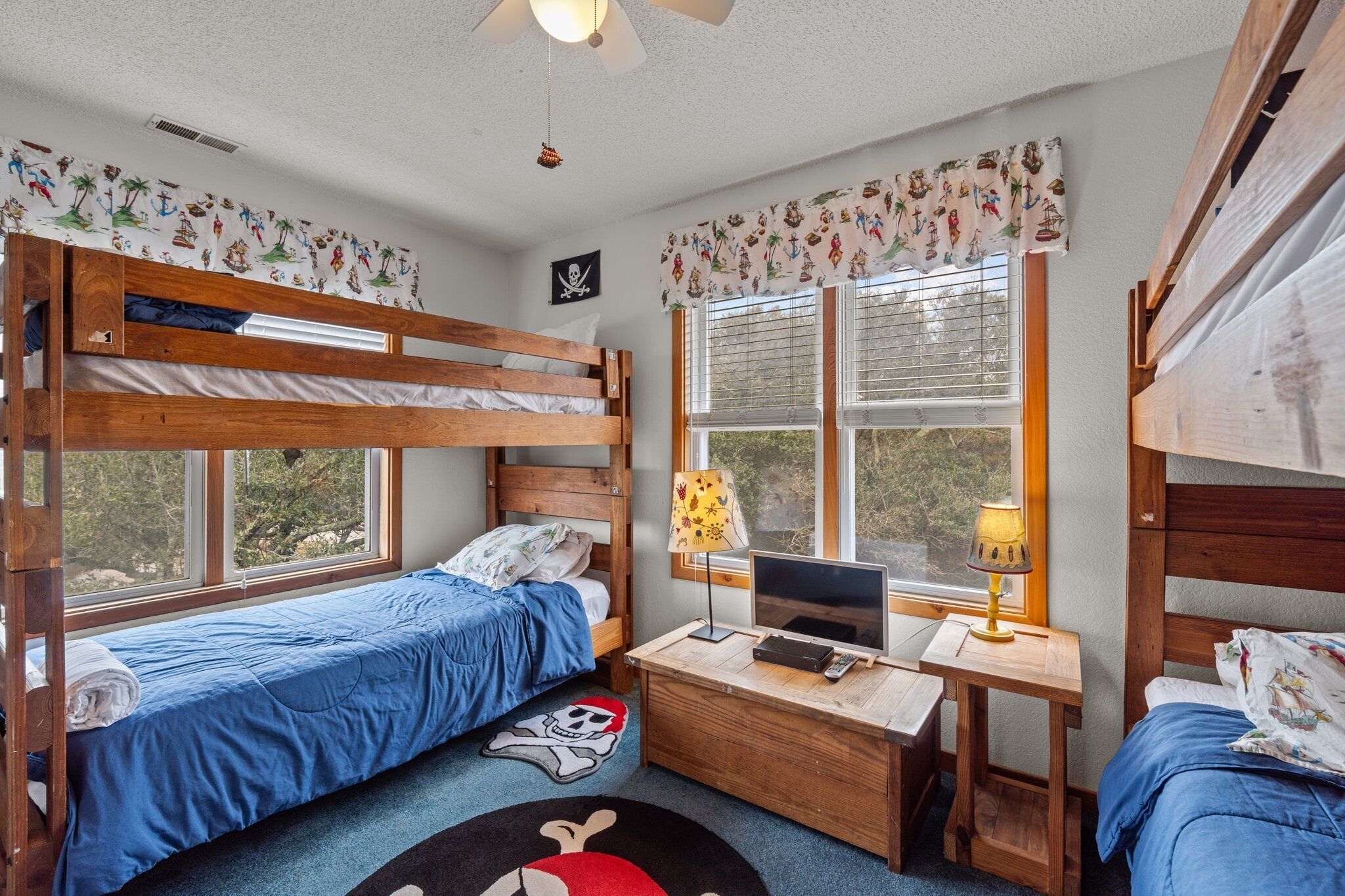 Une chambre de type dortoir, avec des lits superposés, un bureau avec un ordinateur et une fenêtre avec des rideaux.