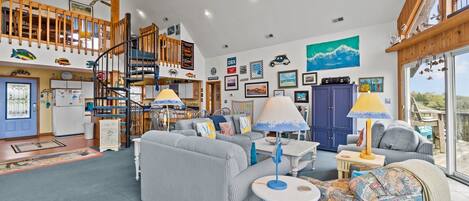A spacious living area with a high ceiling, a staircase, and a balcony with a view.