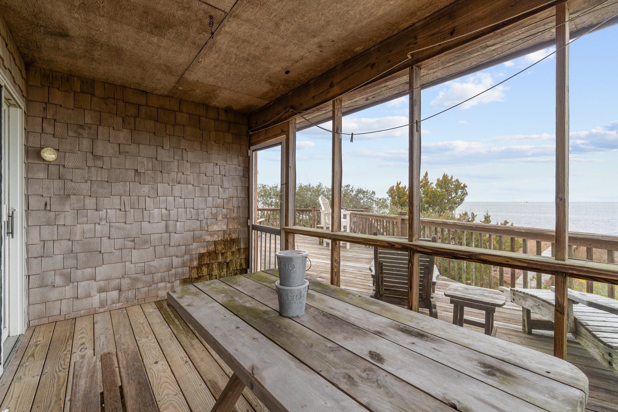 Une terrasse en bois, avec un mur en briques et de grandes fenêtres donnant sur une étendue d’eau.
