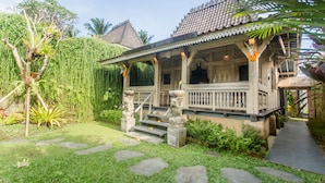 A traditional house with a tiled roof, a porch with stone statues, and a garden with a stone pathway. - Wooden Ganeca Villas by GenuineHost (Tegallalang)