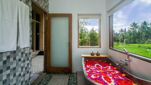 A bathroom with a large bathtub filled with colorful flower petals, a window with a view of greenery, and a checkered wall pattern. - Wooden Ganeca Villas by GenuineHost (Tegallalang)