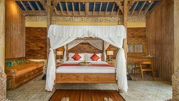 Een hemelbed met houten frame, een witte hemel en rode kussens.