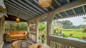 Uma área externa coberta com um banco de madeira, uma mesa e um candeeiro pendente.