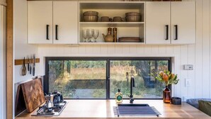 A modern kitchen with white cabinetry, a gas stove, and a large window overlooking a natural landscape.