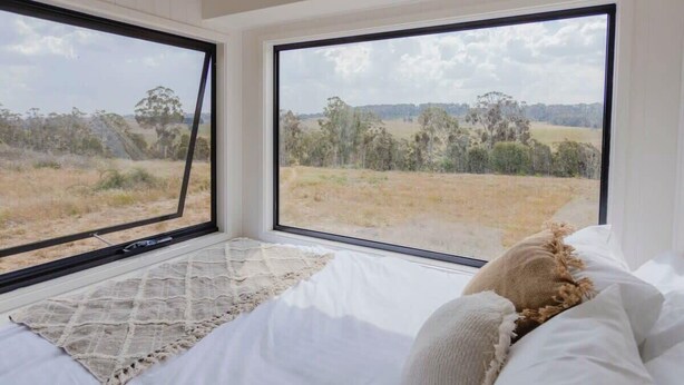 A bedroom with a large window offering a view of a grassy field and trees.