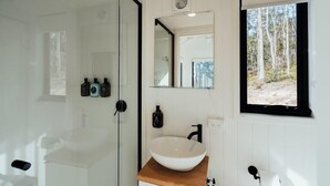 A modern bathroom with a glass shower enclosure, a white sink with a wooden countertop, and a large mirror above the sink.