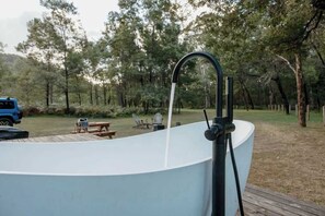 Een groot buitenbubbelbad met een kraan, omgeven door een terras en een picknickplaats.
