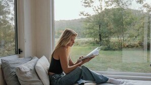 Una persona sentada en una cama junto a una ventana con vistas a un paisaje natural.