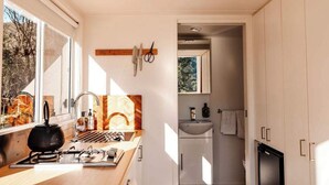Cocina pequeña equipada con estufa a gas, lavamanos y ventana con vista a un jardín.