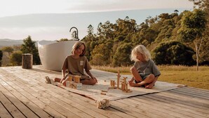 Two people sitting on a wooden deck outdoors with a large bathtub and a map. - Tiny Heidi Summary:<br>T (Bollier)