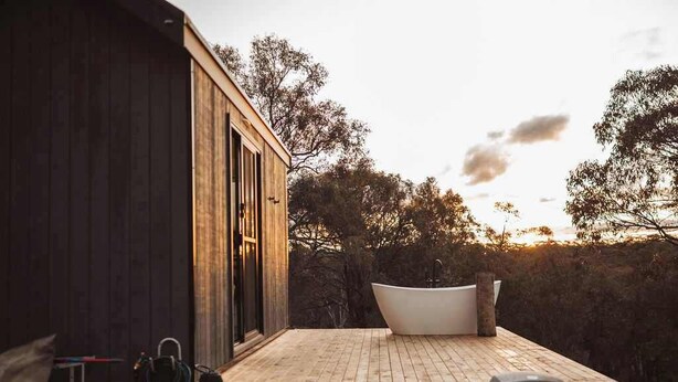 A wooden deck with a bathtub, a grill, and a hose.