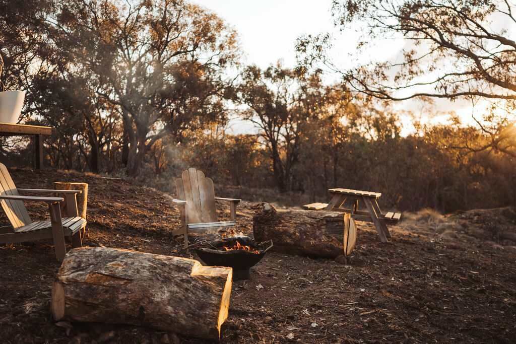 A campsite with a fire pit, wooden chairs, and a table.