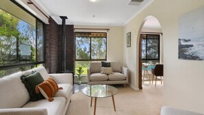 A modern living room with a sofa, a glass coffee table, and a view of a pool and garden through large windows. - Southern Vales by Wine Coast Holiday Rentals (WILLUNGA SOUTH)