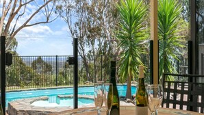 A table with a bottle of wine and two glasses, overlooking a swimming pool with a view of trees and a fence. - Southern Vales by Wine Coast Holiday Rentals (WILLUNGA SOUTH)