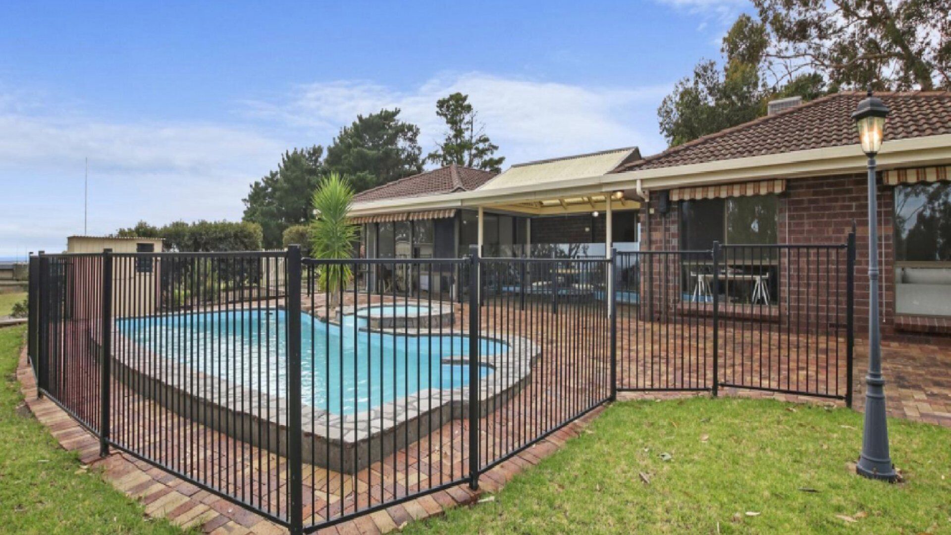 A backyard with a swimming pool, a covered patio, and a brick fence.