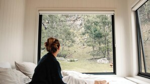 A person sitting on a bed with a window view of a natural landscape.