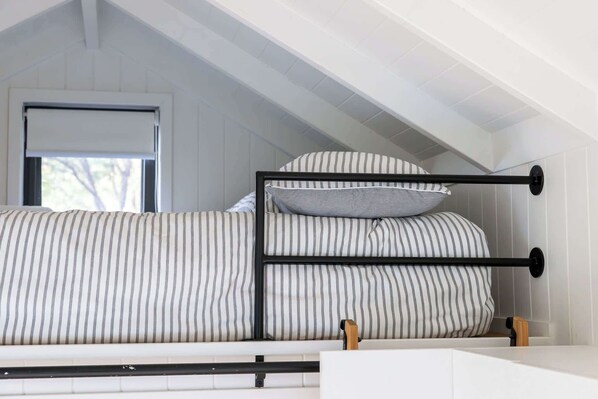 Una cama individual con ropa de cama a rayas, una ventana con persiana y un cabecero de madera.