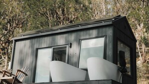 A wooden cabin with large windows, a balcony with chairs, and a speaker.