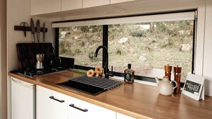 A kitchen with a window, a sink, a coffee maker, a kettle, and a sign.