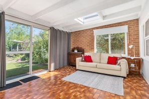 Un salon avec un canapé, un plancher en bois, un mur en briques et une grande fenêtre.