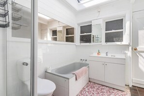 Ein Badezimmer mit Duschkabine, Badewanne, Toilette, Waschbecken mit Spiegel und gefliestem Boden.