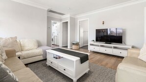 Una sala de estar con sofá, una mesa de centro, un televisor sobre un mueble bajo y un pasillo que conduce a un cuarto de lavado.