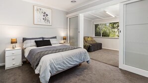 Un dormitorio con cama, mesitas de noche, ventana y puerta corrediza a un balcón.