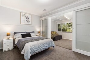 Ein Schlafzimmer mit einem Bett, Nachttischen, einem Fenster und einer Schiebetür, die auf einen Balkon führt.
