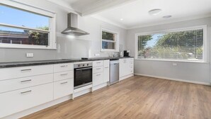Una cocina moderna con armarios blancos, horno empotrado y ventana con persianas.