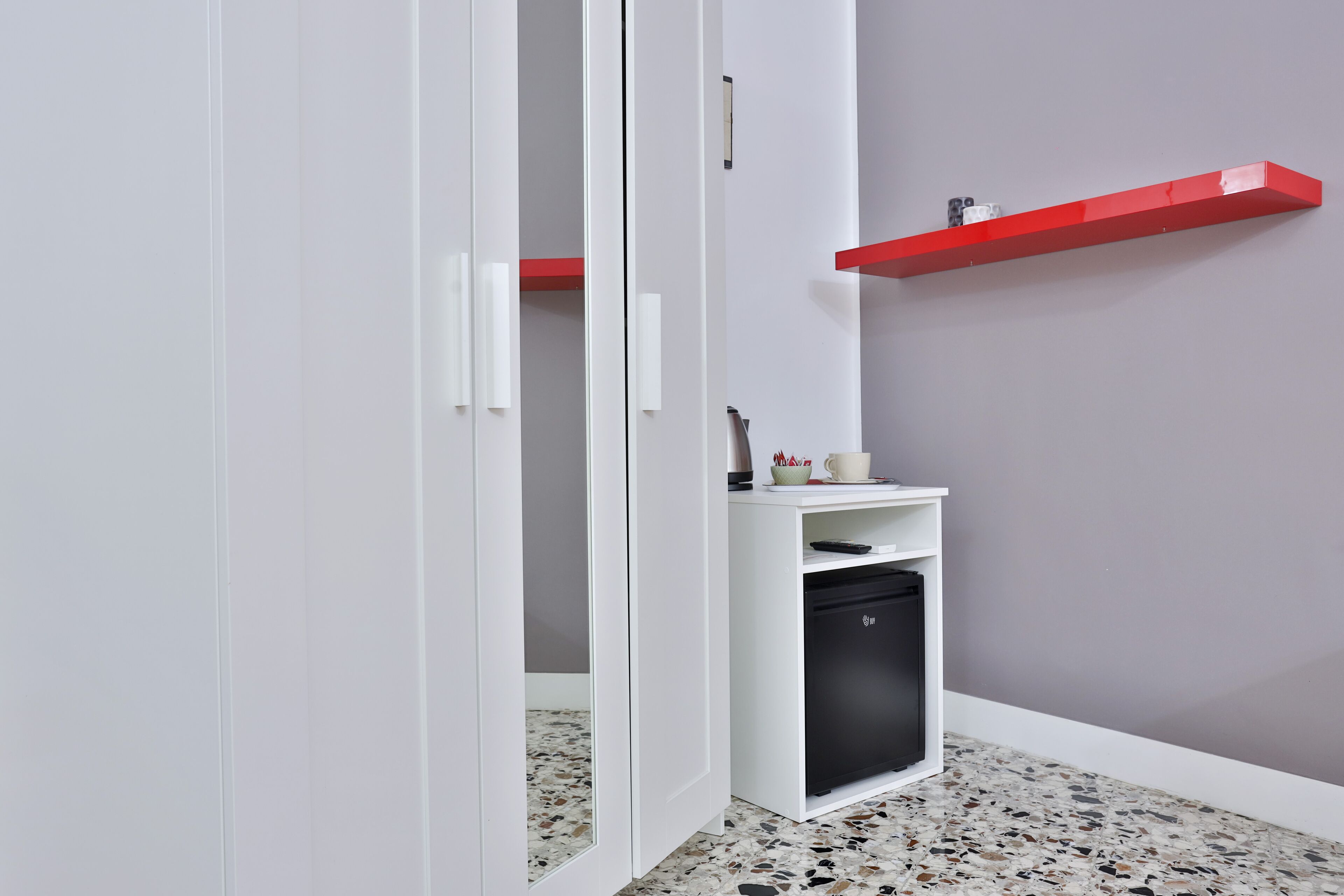 A modern bathroom with a white sink, a black dishwasher, and a red shelf against a grey wall.