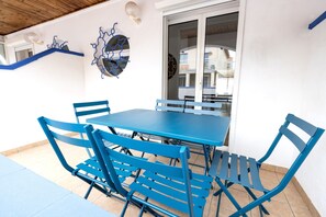 Relax on the patio with a blue table and matching chairs, surrounded by decorative art pieces and a sliding glass door leading to a space.