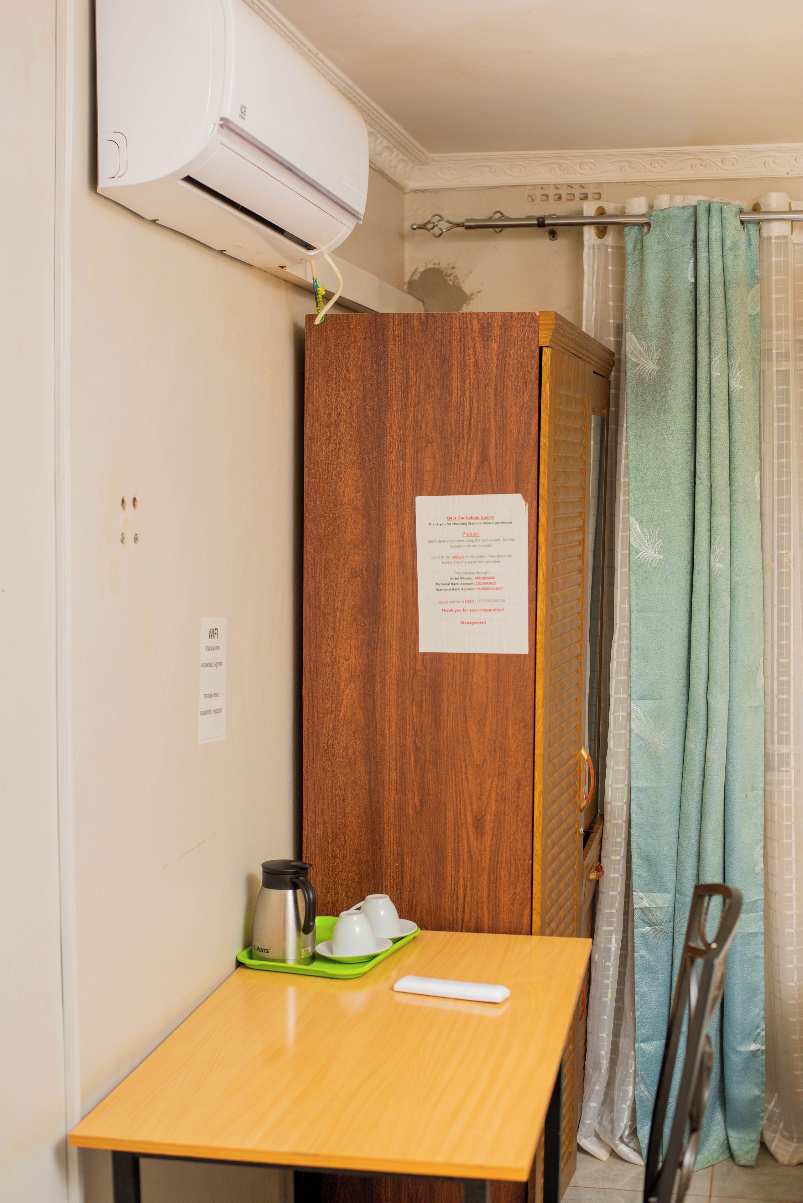 A small room with a wooden wardrobe, a table with a kettle and cups, a shower curtain, and a sign with guest instructions.