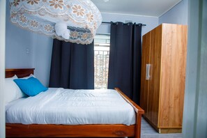 A bedroom with a wooden bed, a large wardrobe, and a window with curtains. - Stadium View Executive Guest House (Lilongwe)