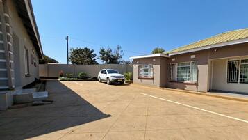 A residential area with a paved driveway, a parked white SUV, and a building with barred windows.