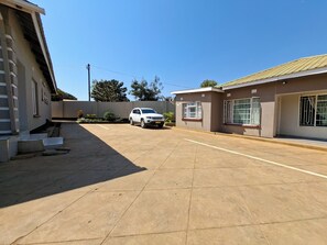 A residential area with a paved driveway, a parked white SUV, and a building with barred windows. - Stadium View Executive Guest House (Lilongwe)