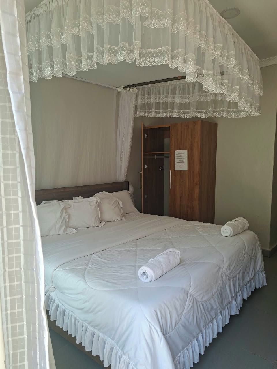 Een slaapkamer met een bed, een houten garderobe en een wit hemelbed.