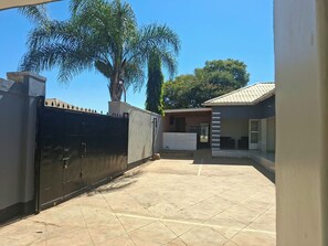 A courtyard with a tiled floor, a black gate, and a building with a tiled roof. - Stadium View Executive Guest House (Lilongwe)