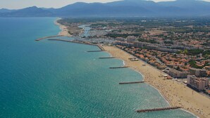 An aerial view of a coastal city with a long beach, a marina, and residential buildings.
