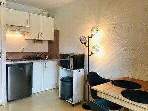 A compact kitchen with a dishwasher, microwave, and a small trash bin.