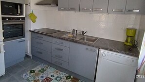 A compact kitchen with grey cabinets, a built-in oven, a dishwasher, and a sink. - Spacious apartment in Argelès, terrace + private parking (Argelès-sur-Mer)