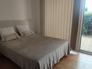 A bedroom with a bed, two pillows, a window with blinds, and a view of the outside.