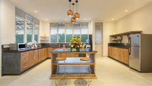 A modern kitchen with a central island, wooden cabinets, stainless steel appliances, and pendant lighting. - Villa Hasian Jimbaran (Jimbaran)