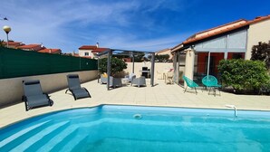 A swimming pool with lounge chairs, a covered patio area, and a view of houses in the background. - Air-conditioned house with pool, parking, and WIFI - 6 pers. (Argelès-sur-Mer)