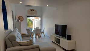 A modern living room with a grey sectional sofa, a flat-screen TV on a white console, and a dining area with a glass table and chairs. - Air-conditioned house with pool, parking, and WIFI - 6 pers. (Argelès-sur-Mer)