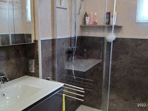 A bathroom with a shower enclosure, a sink, and a shelf with toiletries.