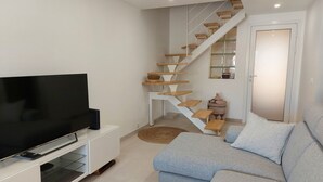 A modern living room with a flat-screen TV on a white entertainment unit, a light blue sofa, and a wooden staircase with a basket on the landing. - Air-conditioned house with pool, parking, and WIFI - 6 pers. (Argelès-sur-Mer)