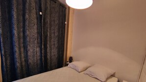 Un dormitorio con cama, almohadas blancas, mesita de noche, lámpara y cortinas estampadas.