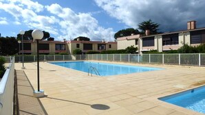 A swimming pool with a tiled deck, surrounded by a white fence, and buildings in the background.